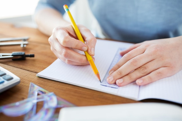 school, education, people and learning concept - close up of student or woman hands with ruler and pencil drawing line in notebook