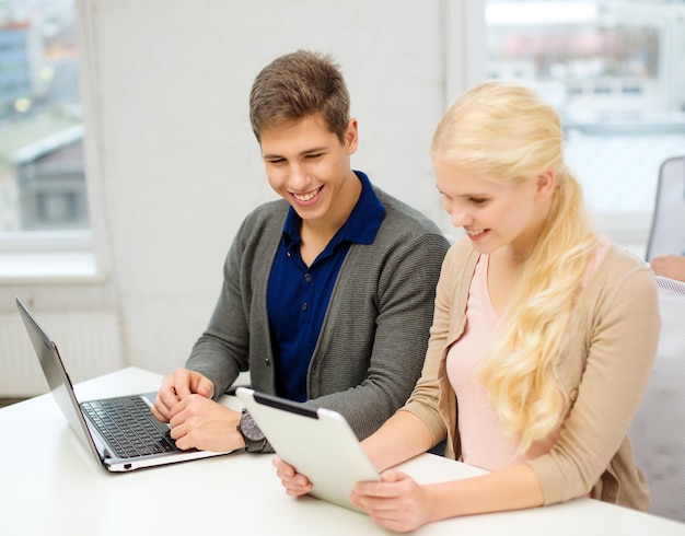 school, education, technology and internet concept - two teens with laptop and tablet pc at school