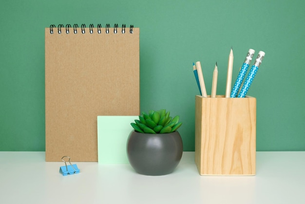 School equipment on white table green wall background Education backdrop Wooden school supplies notepad pencils and cactus plant Back to school Student Desk Stationery for study Work at home