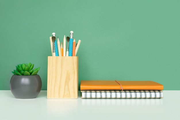 Photo school equipment on white table green wall background education backdrop wooden school supplies notepad pencils and cactus plant back to school student desk stationery for study work at home