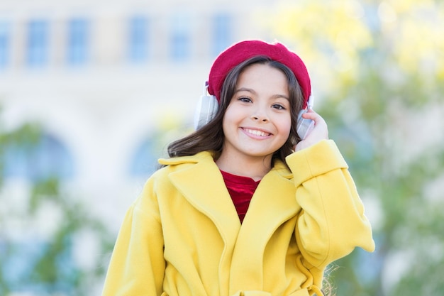 学校の秋のシーズンの小さな女の子は、ヘッドセットでオーディオブックの小さな女の子を聞くオンライン教育音楽愛好家の電子ブックテクノロジーフランスのベレー帽の秋のファッションで陽気なパリジャンの女の子答えへのあなたのガイド