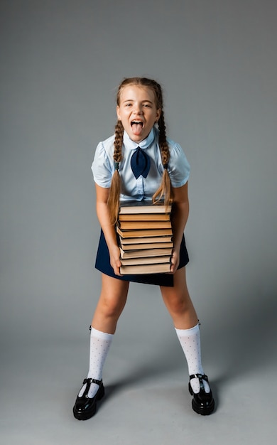 School girl holding heavy textbooks on yellow studio background