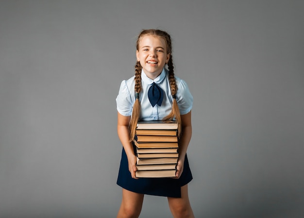 School girl holding heavy textbooks on yellow studio background