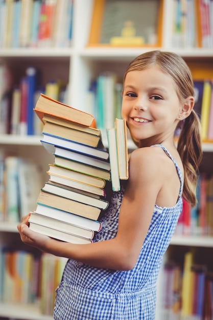 School girl holding stack of books in library