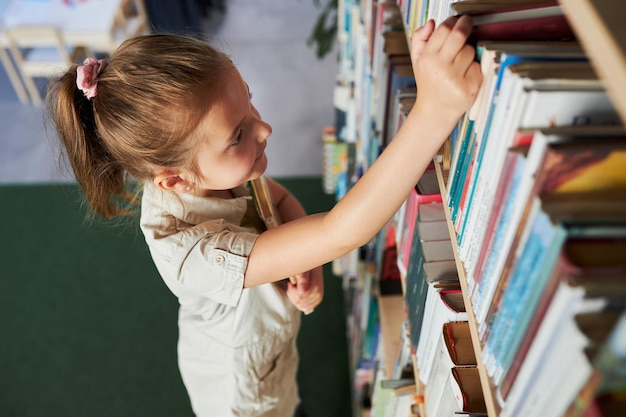 Школьница смотрит на книжную полку в школьной библиотеке умная девушка выбирает литературу для чтения