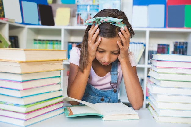 Ragazza della scuola che legge un libro in biblioteca