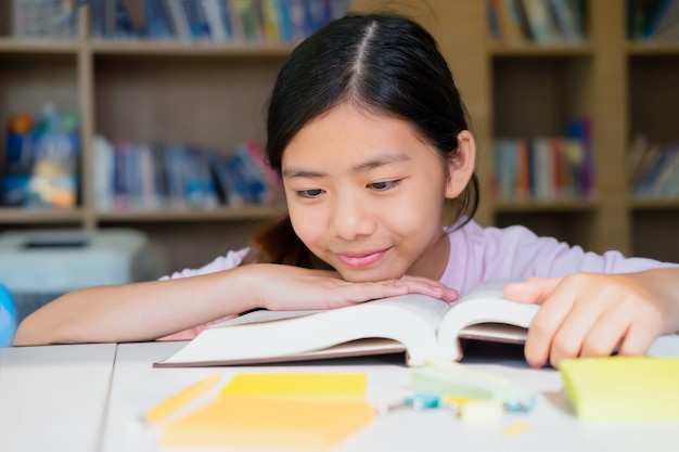 Школьная девочка читает книгу в библиотеке.
