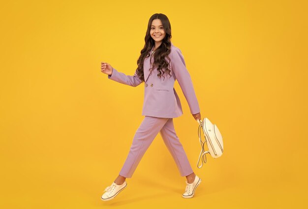 School girl in school uniform with school bag schoolchild\
teenager hold backpack on yellow isolated background happy face\
positive and smiling emotions of teenager girl