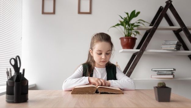 School girl sitting indoors and reading a thick old book\
quickly turning the pages a gentle pensive child learns online\
remotely at home completing the teacher\'s assignments