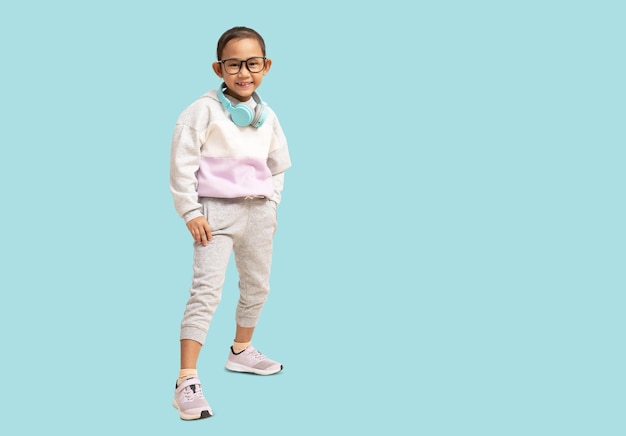 School girl smiling Asian student school kid wearing headphones standing Full body portrait isolated on pastel plain light blue background