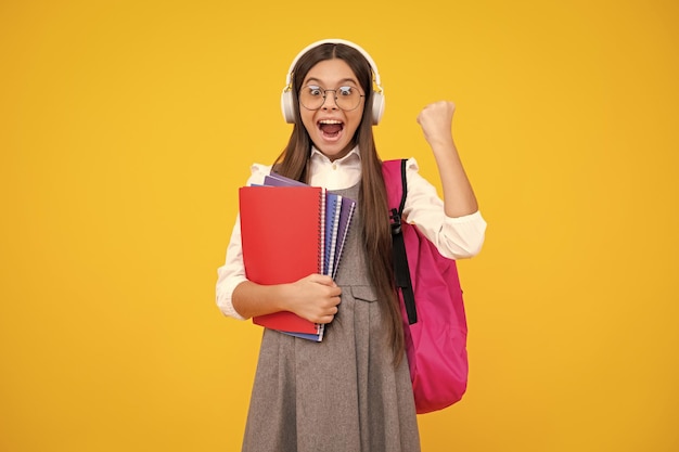 School girl teenage 12 13 14 years old in headphones and books on isolated studio background school kids with backpack excited teenager girl