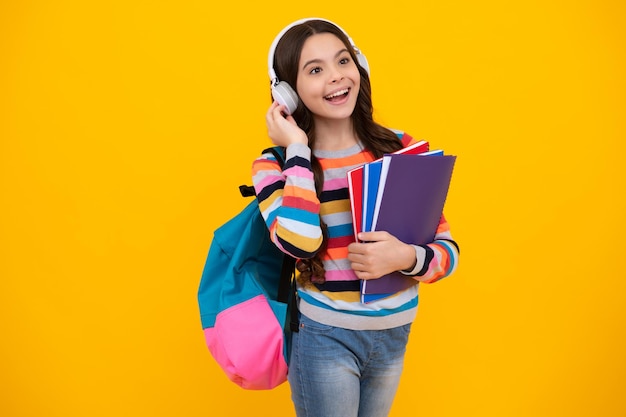 School girl teenage student in headphones hold books on yellow isolated studio background School and music education concept Happy teenager positive and smiling emotions of teen girl