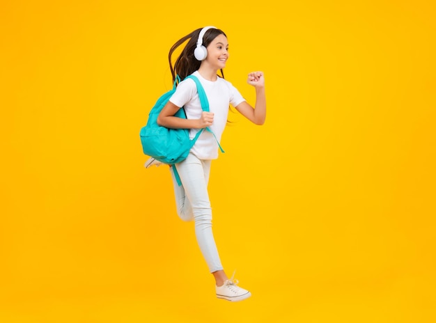 School girl teenager student in headphones on yellow isolated studio background School and music