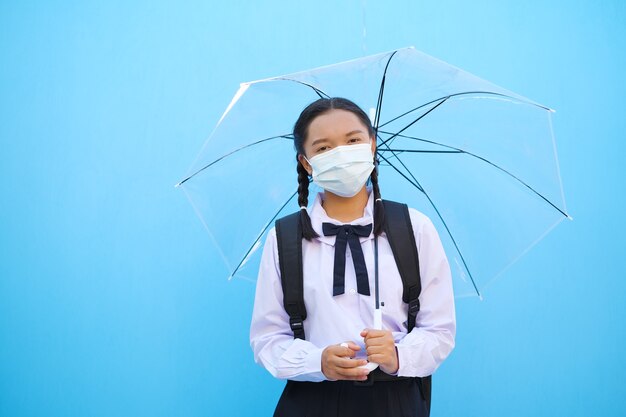 여학생은 파란색 배경에 우산이 있는 마스크를 착용합니다.