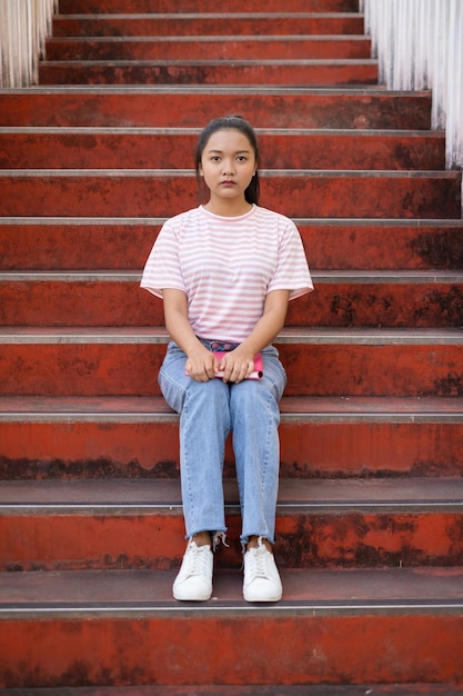 School girl  wear pink shirt and jean holding and holding pink book on stairs.