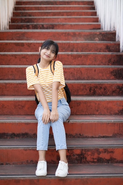 School girl  wear pink shirt and jean holding and holding pink book on stairs