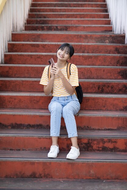 School girl  wear pink shirt and jean holding and holding pink book on stairs