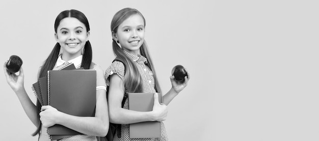 School girls friends Happy pupils with books hold vitamin organic apples yellow background school