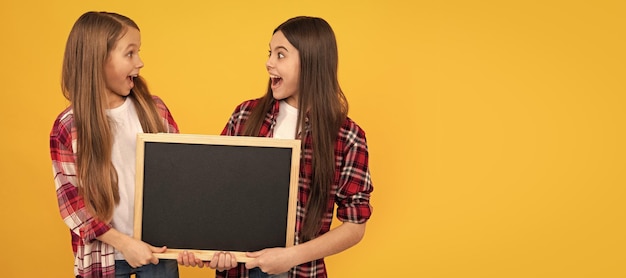 School girls friends shocked kids in casual checkered hold school blackboard copy space promotion