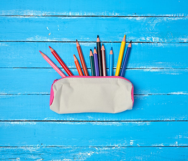 School gray textile pencil case and scattered multicolored wooden pencils 