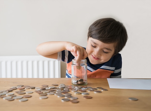 透明な瓶にお金のコインを入れる学校の子供