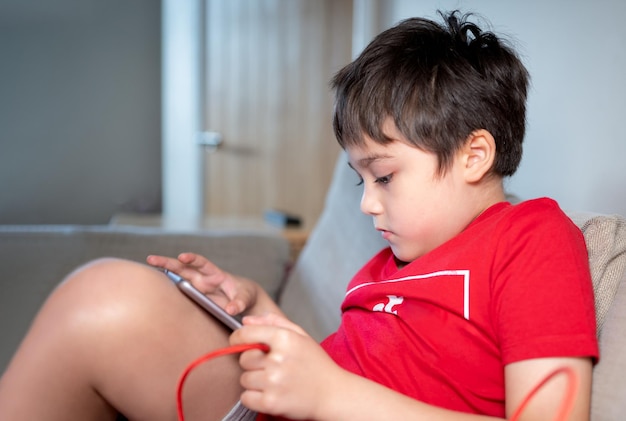 태블릿을 사용하는 학교 아이가 인터넷에서 준비하는 이야기 소파에 앉아 온라인 학습을 하는 행복한 소년 집에서 디지털 패드를 들고 와이파이를 사용하여 게임을하거나 친구들과 채팅하고 있습니다.