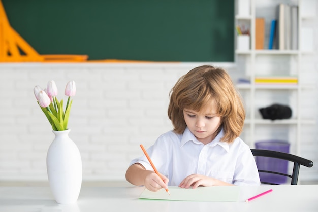 コピーブックに書き込み、教室のテーブルに座っている学校の子供。一年生。