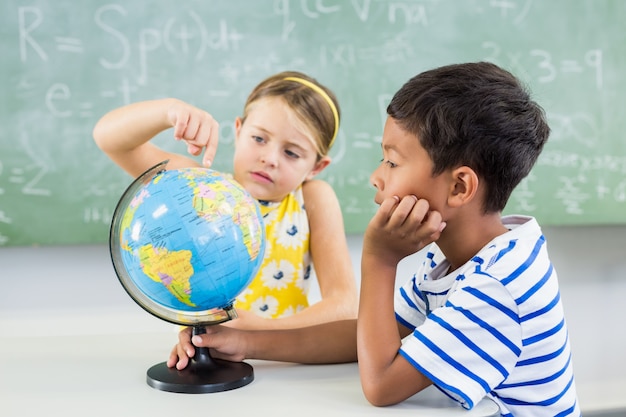 School kids looking at globe in classroom