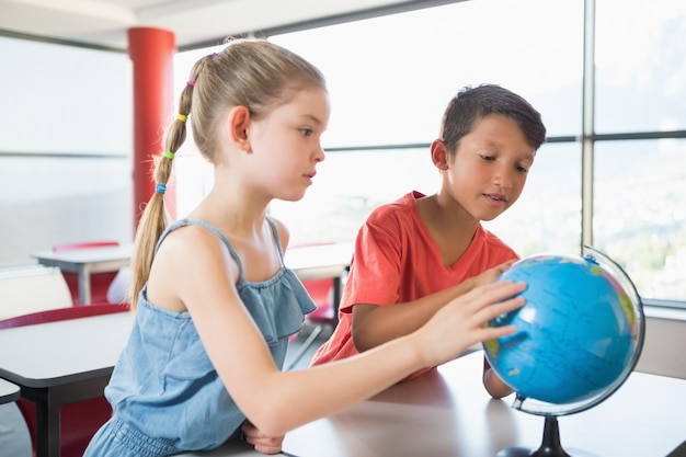 School kids looking at globe in classroom