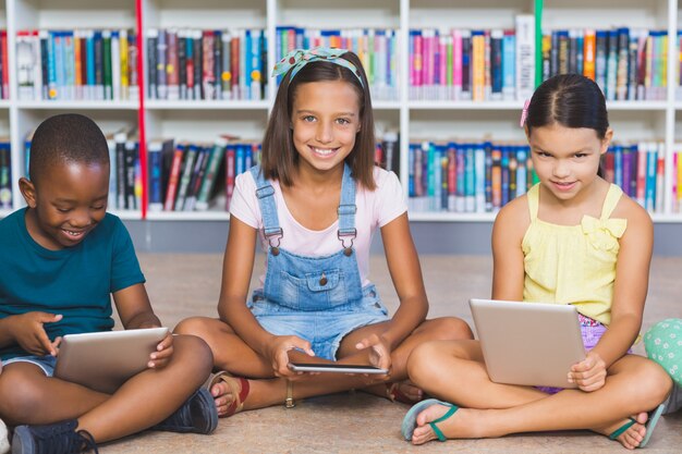 School kids sitting on floor using digital tablet in library