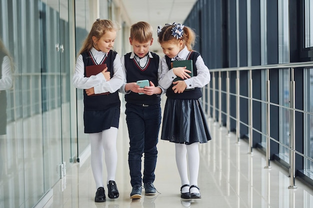 School kids in uniform together with phone in corridor Conception of education