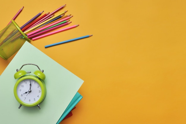 School levert boeken, potloden en een wekker op een gele achtergrond