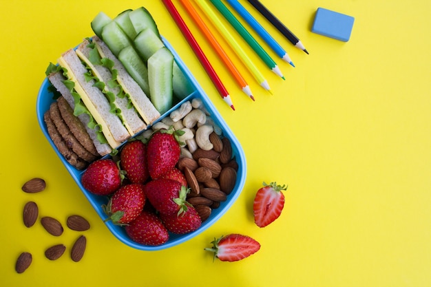 School lunch in the blue box and school stationery  on the yellow background. Top view. Copy space.