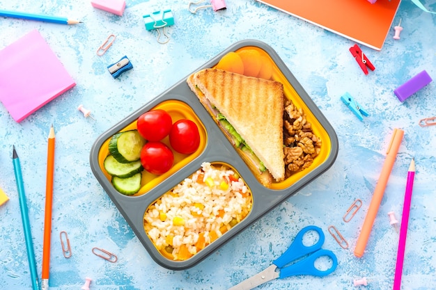 Photo school lunch box with tasty food and stationery on color