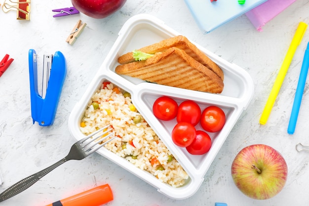 School lunch box with tasty food and stationery on table