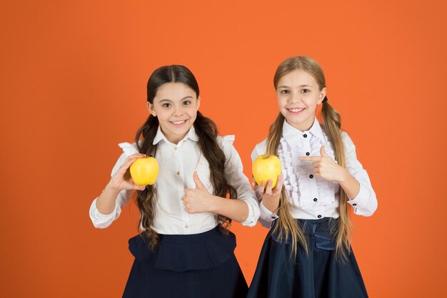 School lunch Vitamin nutrition during school day Boost student acceptance of fruit Distributing free fresh fruit at school Girls kids school uniform orange background Schoolgirls eat apples