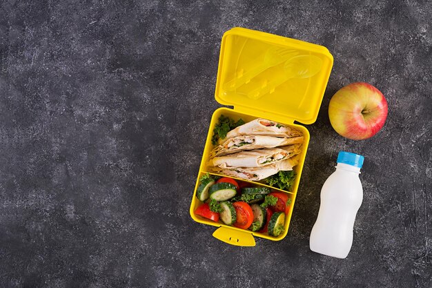 School lunchbox. Healthy lunch box with tortilla wraps stuffed chicken fillet, cheese and tomatoes and fresh salad. Top view, flat lay