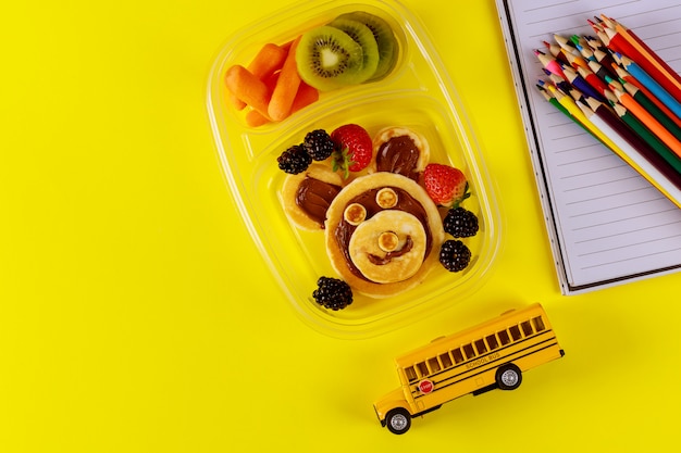 School lunchbox met pannenkoeken, vers fruit en schoolbus speelgoed.