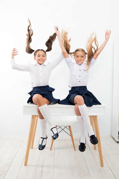 School pauze concept. het schattige kapsel van schoolmeisjes zit op het bureau. beste vrienden hebben gratis plezier om met haar te spelen. perfecte schoolmeisjes met netjes fancy haar. schoolkapsels paardenstaarten in de lucht.