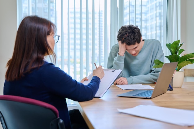 School psychologist supporting guy student sitting in office of educational building