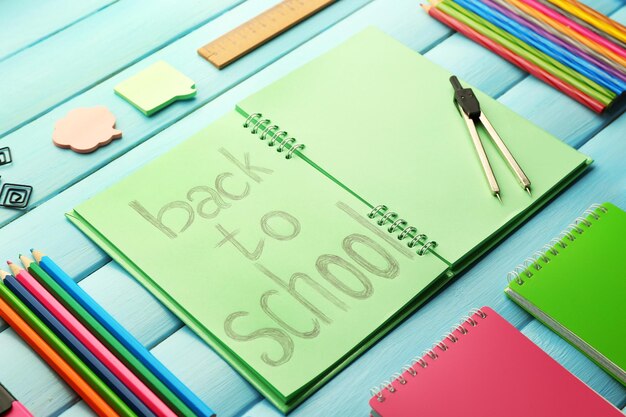 Foto set scuola con iscrizione di ritorno a scuola in quaderno e cancelleria su sfondo blu in legno