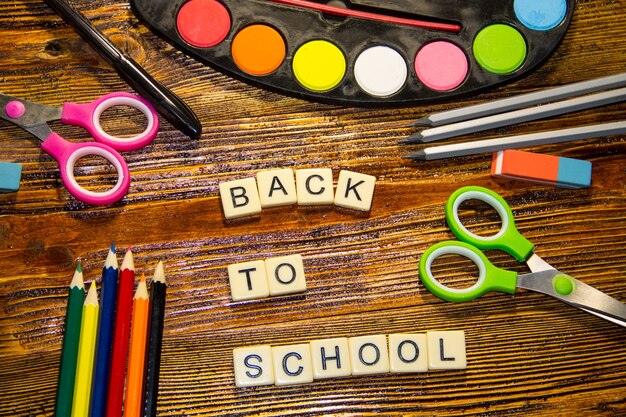 Foto set scuola con iscrizione di ritorno a scuola, matite, penna, forbici, gomma e colori ad acquerello su scrivania in legno