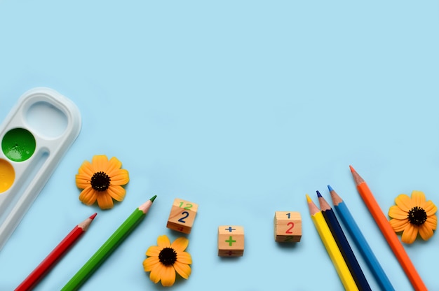 School set with pencils, paints, paper clips, brushes, scissors, autumn flowers on a blue background 