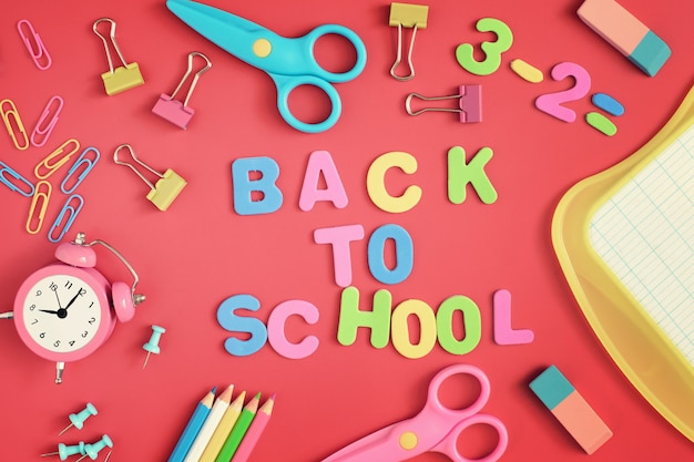 Photo school and stationery are scattered on the red background. in the center of the inscription in colored letters, back to school.