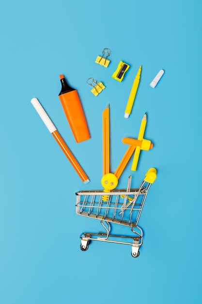 Photo school stationery and mini trolley on a blue background concept back to school study concept stationery shop concept flat lay top view vertical photo