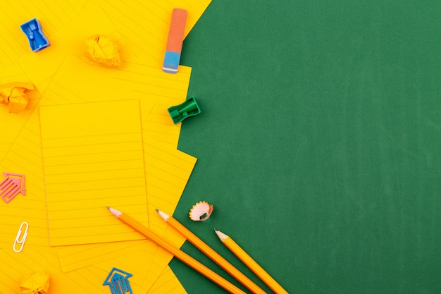 School stationery and orange sheet of paper lie on the green school board forming a frame for text. near pencil and crumpled pages. Copy space Flat lay Top view Concept Education