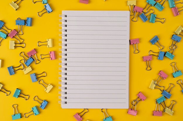 School stationery and paper notebook on yellow background with paper clip top view copy space