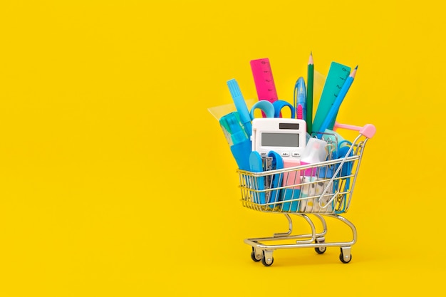 School stationery in a shopping cart on a yellow background Back to school concept