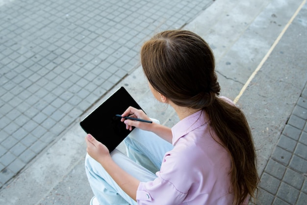 Una studentessa sui gradini della scuola con un gadget in mano education generation z