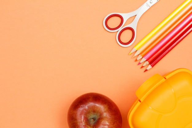 School supplies. Apple, scissors, color pencils and lunch box on pink background. Top view with copy space. Back to school concept. Pastel colors